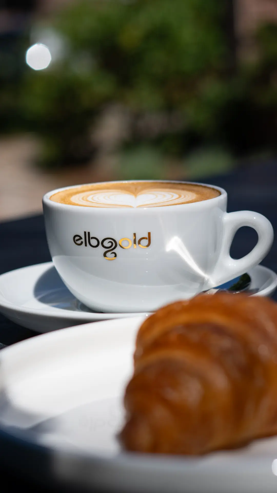 elbgold-Cappuccino mit Croissant im Sonnenlicht